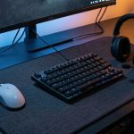 Configuration e-sport FPS réaliste sur un bureau sombre avec souris légère, clavier TKL, grand tapis en tissu et casque avec microphone, éclairage discret.