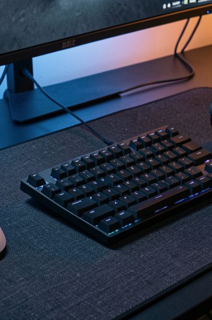 Configuration e-sport FPS réaliste sur un bureau sombre avec souris légère, clavier TKL, grand tapis en tissu et casque avec microphone, éclairage discret.